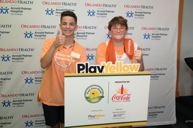 Two teenagers smiling behind a Golf Fore Good sign